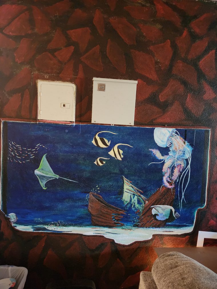 Earlier capture of the painted aquarium: the manta ray, moorish idol fish, jellyfish and sunken shipwreck already in place on the blue ground, set into a wall of red-brown painted rock.