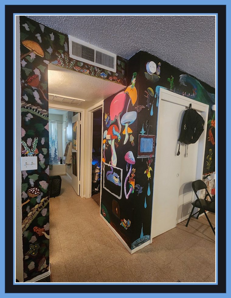 Corner view where the mushroom wall meets a forest-and-vine mural running down the hallway wall, painted with toadstools, leaves and small animals on black.