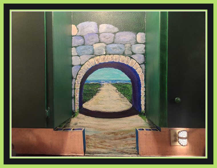 Trompe-l'oeil stone archway painted between two green doors, a tunnel of grey and lavender blocks opening onto a sand path that runs to a grassy shore and the sea, with terracotta planter ledges at the base.