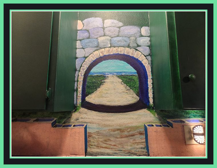 Closer head-on view of the same painted archway, the sand path and ocean horizon visible straight through the tunnel.