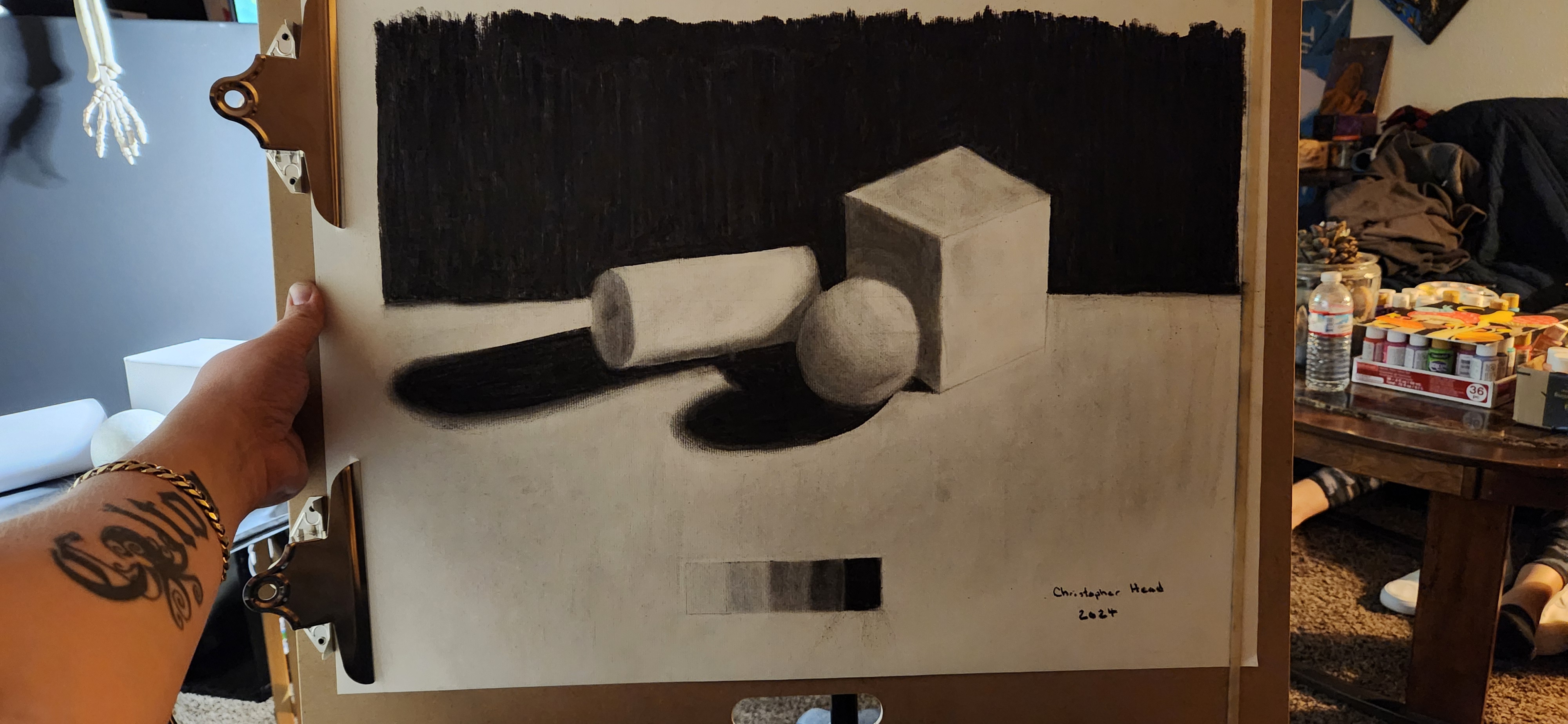 Charcoal still-life value study of three geometric forms, a cube, cylinder, and sphere, casting deep shadows against a dark backdrop.